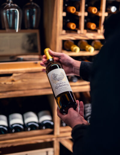 Man holding wine bottle in a wine room from Vinteknikk, surrounded by Caverack wine shelves in charred pine and WineGuard glass system with matt black frame and warm lighting.